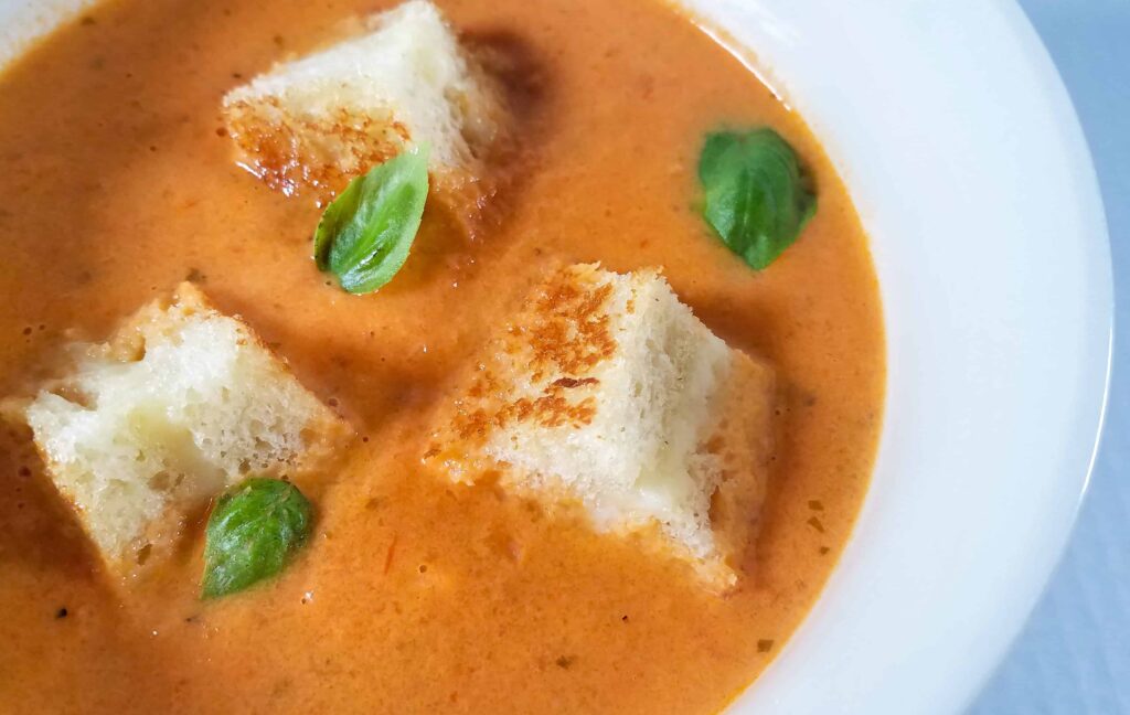 A horizontal close up of creamy tomato bisque with three grilled cheese croutons.