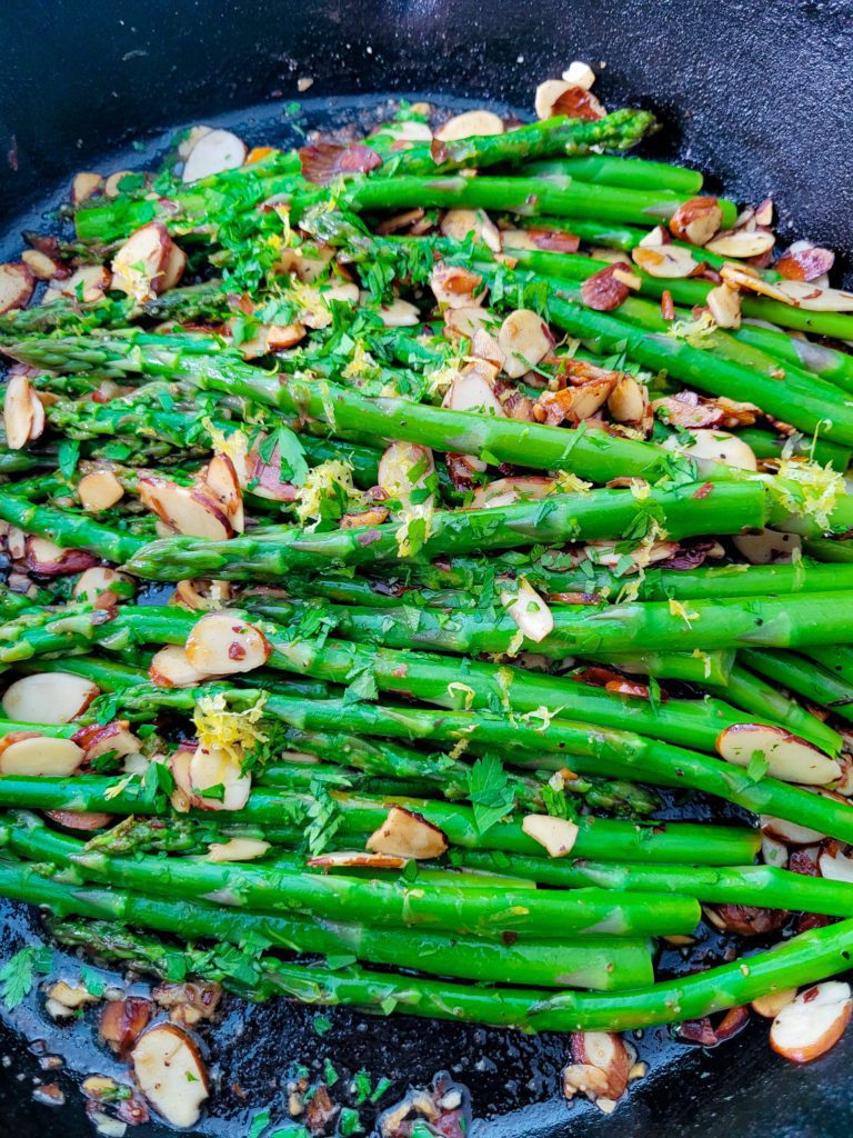 A close up of asparagus amandine in a cast iron skillet.