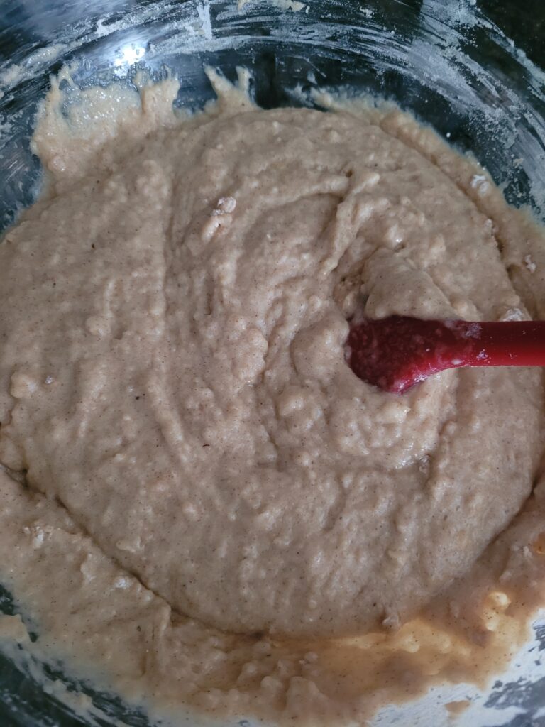 Red spatula mixing wet and dry ingredients for apple upside down bundt cake