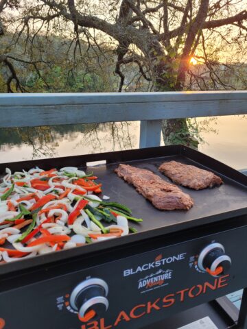 steaks, onions, and peppers on a Blackstone griddle at sunset