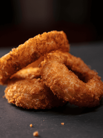 A pile of three onion rings against a dark background